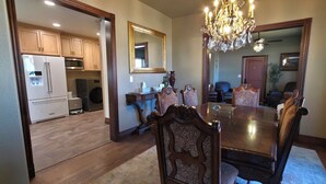 Une salle à manger avec une table et des chaises en bois, un lustre et une cuisine en arrière-plan.