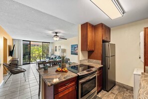 A modern kitchen with a central island, a dining area with a table and chairs, a refrigerator, and a ceiling fan. - Maui Getaway | Walk to Beach, Pool & Hot Tub (Kihei)