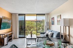 A modern living room with a balcony, a flat-screen TV, a dining table with chairs, and a sofa. - Walk to Beach! Steps to Shops & Dining (Kihei)