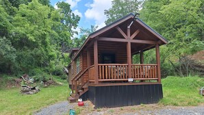 A wooden cabin with a porch, surrounded by trees.