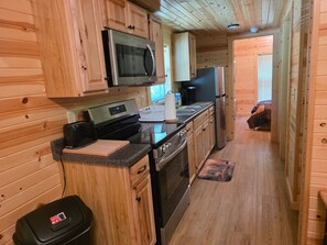 A compact kitchen with wooden cabinetry, a microwave, a refrigerator, an oven, and a sink.
