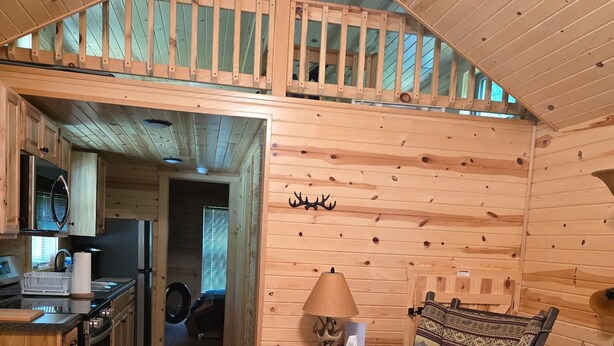 A wooden cabin interior with a kitchen, dining area, and a loft bedroom.