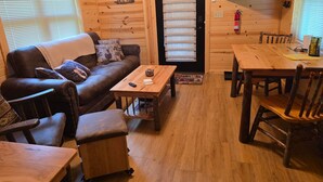 A cozy cabin interior with a sofa, a small table, a dining table, and a TV mounted on the wall.