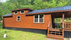 A wooden cabin with a porch, a small deck, and a window.