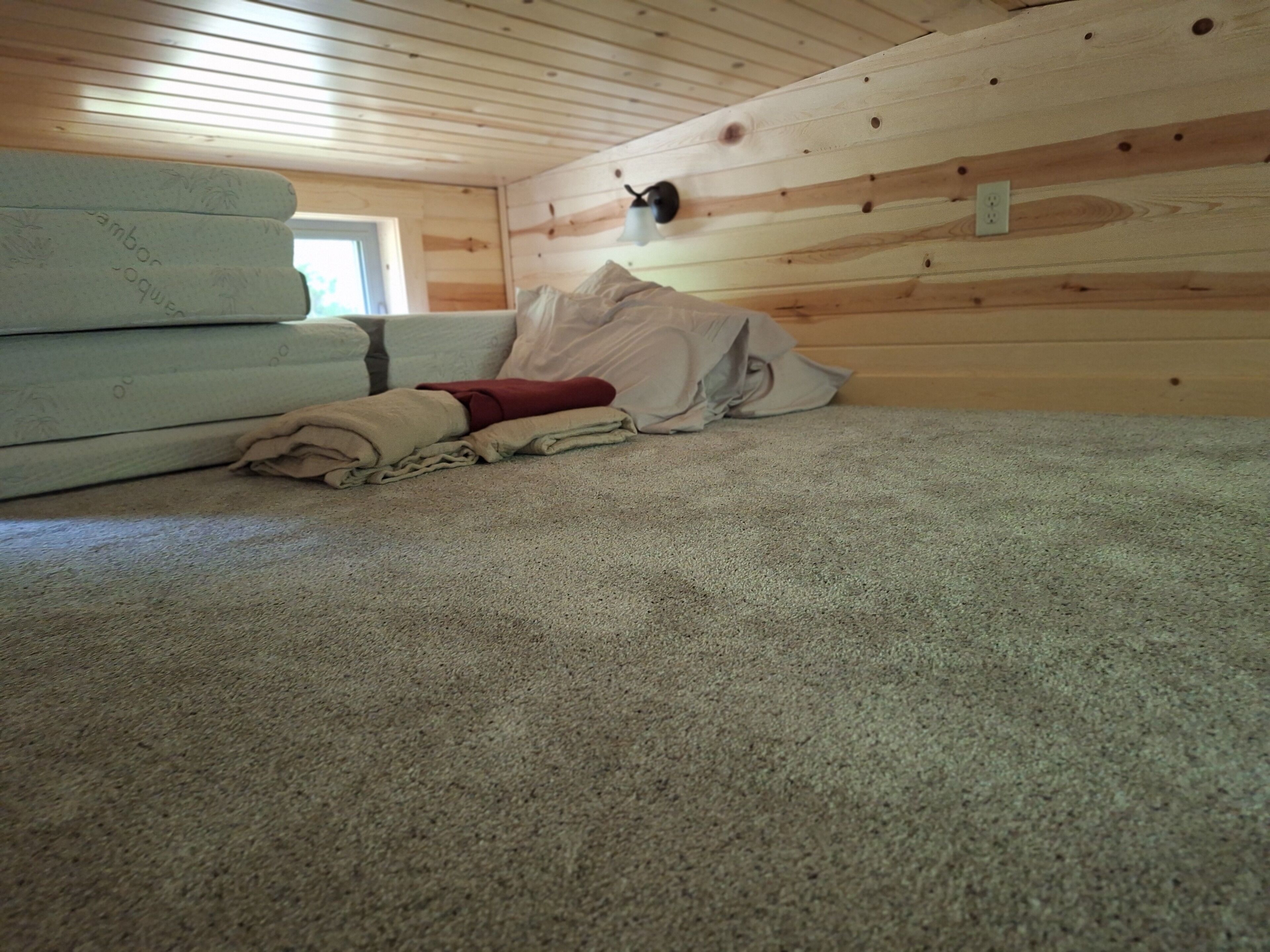 Una habitación con techo de madera, una cama con cubrecama blanco y una ventana pequeña.