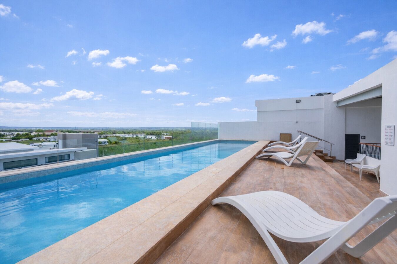 Una piscina en la azotea con vistas despejadas del paisaje circundante, una terraza de madera y sillones blancos.