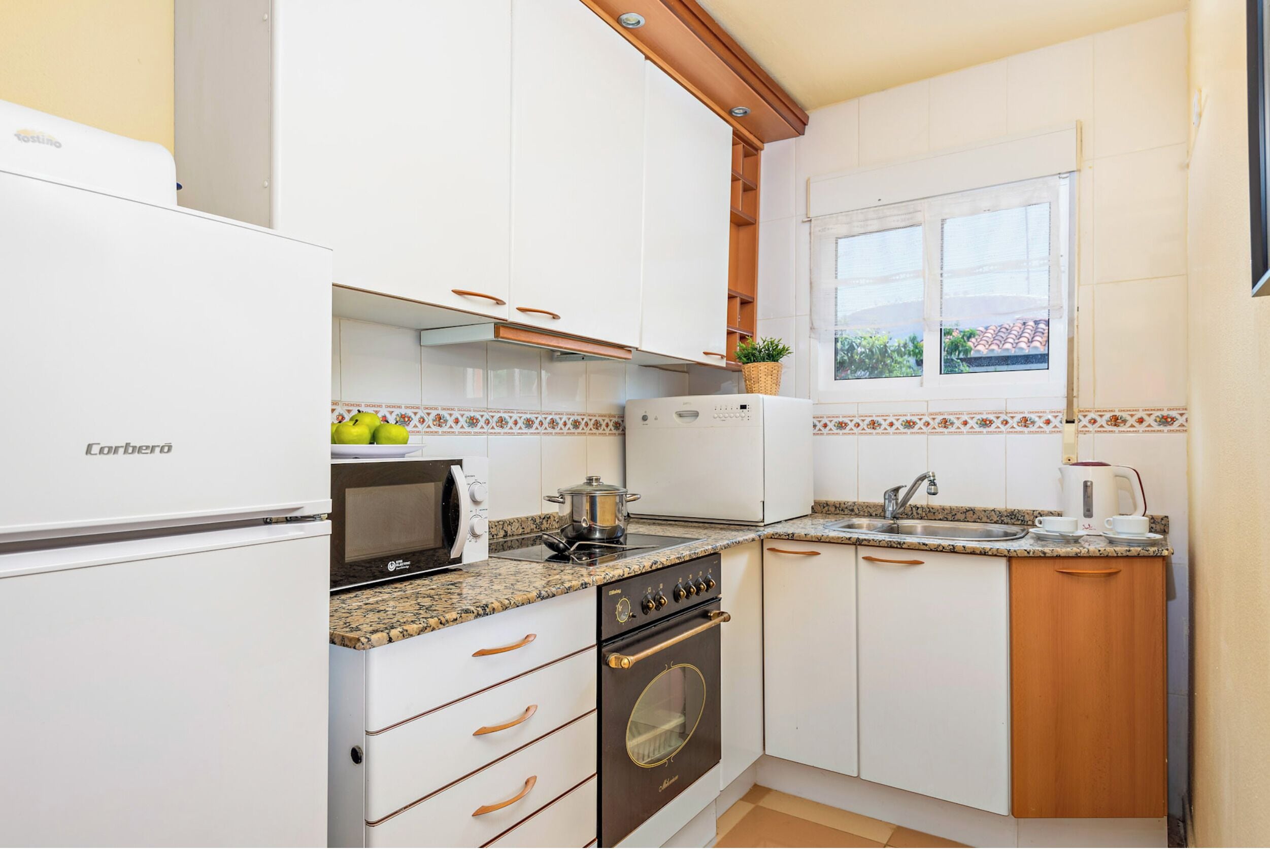 A compact kitchen with white cabinets, a stove, a microwave, and a sink.
