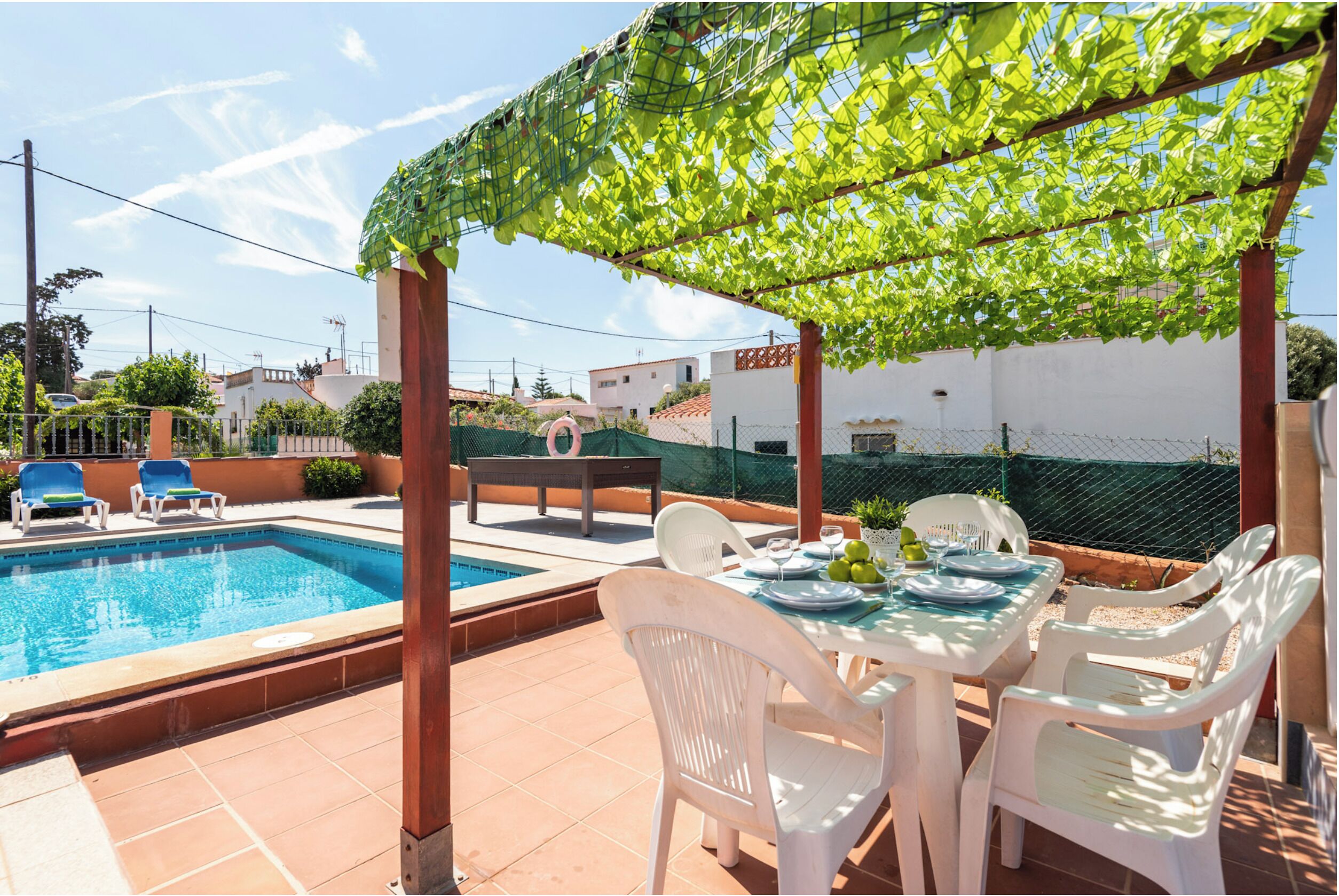 Un espace aménagé au bord de la piscine, comprenant un coin salon couvert, une table dressée pour les repas et une piscine.