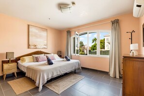 Un dormitorio con cama, mesitas de noche, ventana con cortinas y vistas al exterior.