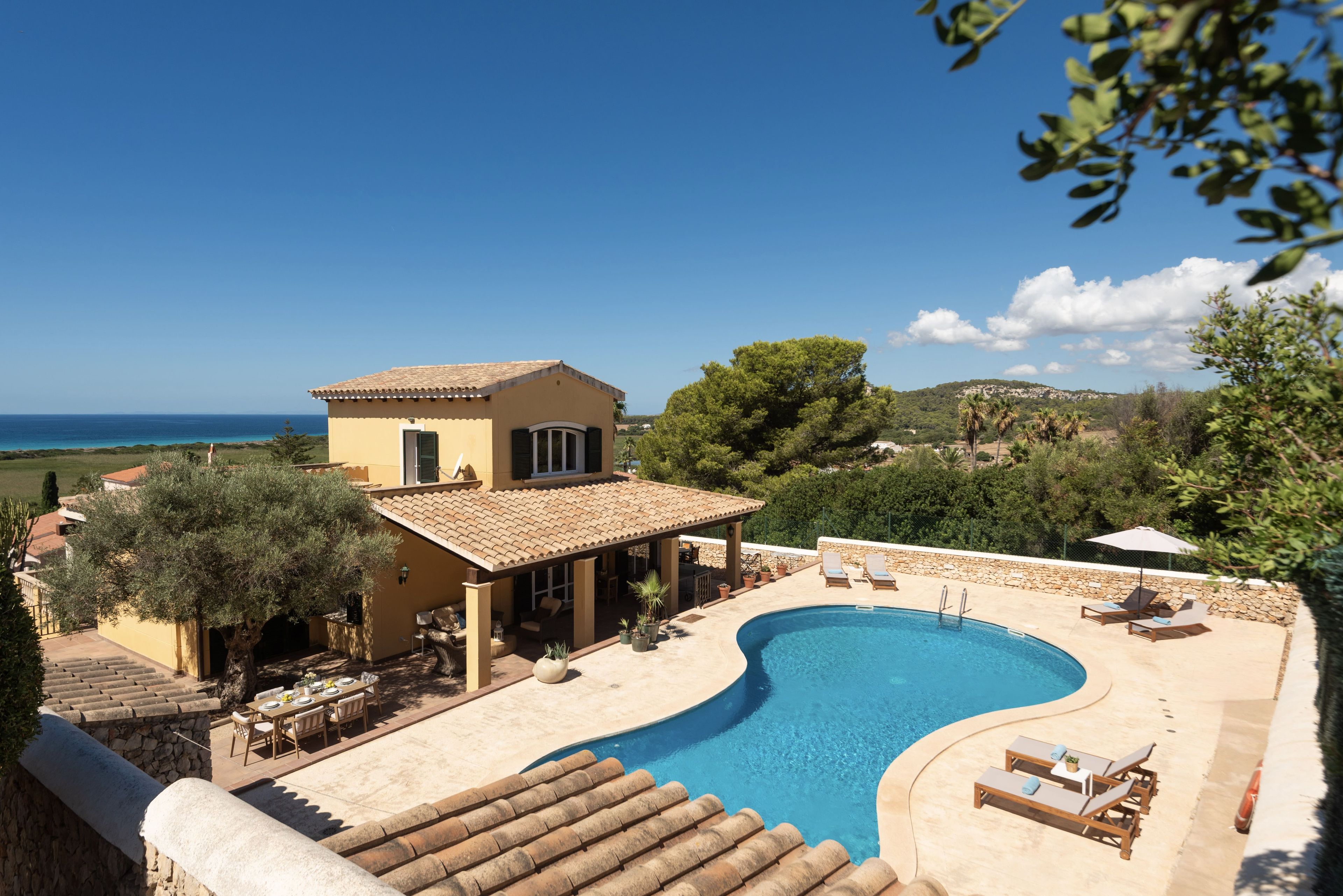 A villa with a swimming pool, outdoor seating, and a view of the sea.