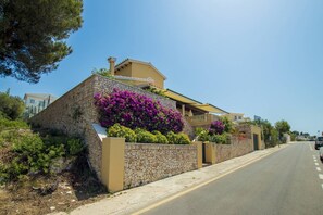 A coastal building with a stone facade, a balcony, and vibrant purple flowers. - Villa Lamar - Three Bedroom Villa, Sleeps 6 (Alayor)