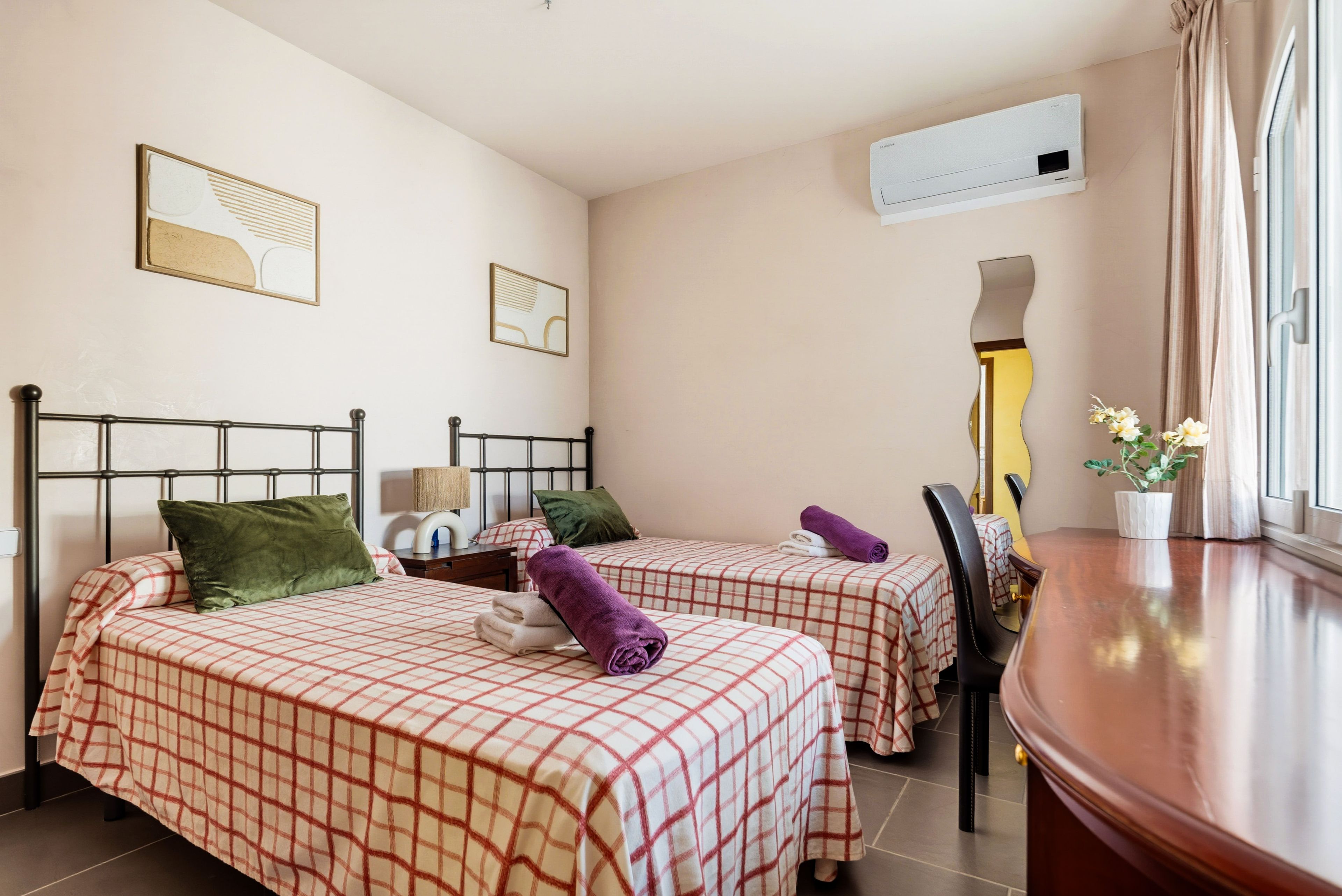 A hotel room with two beds, a wooden side table, a mirror, and a potted plant.