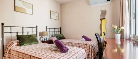 Habitación de hotel con dos camas, una mesita de madera, un espejo y una planta en maceta.