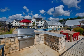 An outdoor patio with a grill, stone walls, a pool, and lounge chairs.