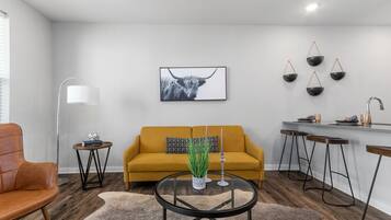Un salon moderne avec un canapé, une table basse et un coin repas équipé de tabourets.