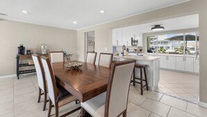 Une cuisine moderne avec des meubles blancs, une table à manger en bois et une vue sur l’extérieur.