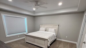 Ein Schlafzimmer mit Bett, Deckenventilator, Fenster mit Jalousien und Teppichboden.