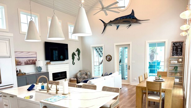 Une cuisine moderne dotée d’un îlot central, un coin repas avec des meubles en bois et un espace de vie comprenant un canapé et des décorations représentant des hippocampes.
