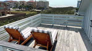Une terrasse en bois avec deux chaises longues et une rambarde blanche.