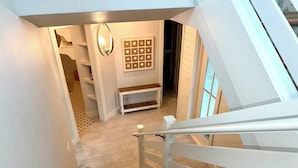 Un escalier avec des rampes blanches menant à une pièce dotée d’un plancher en bois, d’un luminaire fixé au mur et d’un tableau encadré.