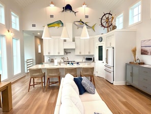 Una cocina moderna con armarios blancos, una isla central con taburetes, un refrigerador y peces decorativos en el techo.