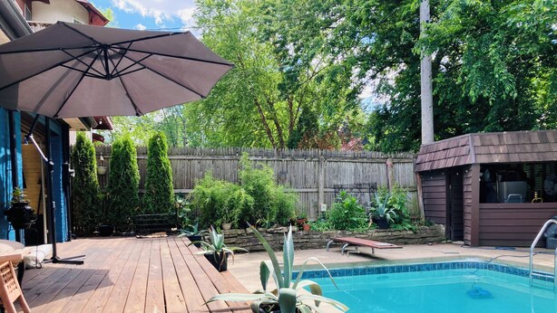 Una terraza de madera con piscina, rodeada de plantas en macetas y una valla de madera.
