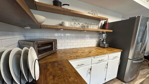 Una cocina con encimera de madera, armarios blancos, horno empotrado y refrigerador de acero inoxidable.