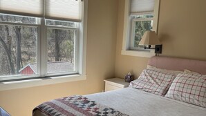 Ein Schlafzimmer mit einem Bett, einem Nachttisch, einer Lampe und einem Fenster mit Jalousien.