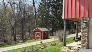 Ein rotes Bauernhaus mit weißer Tür, umgeben von einer Wiese und Bäumen.