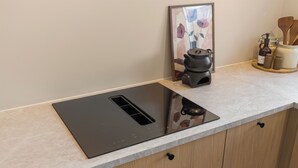 A kitchen with a modern induction cooktop, wooden cabinets, a framed floral artwork, and a spice rack. - Modern 3BR apartment | Free parking | 10 min to centrum (Trondheim)