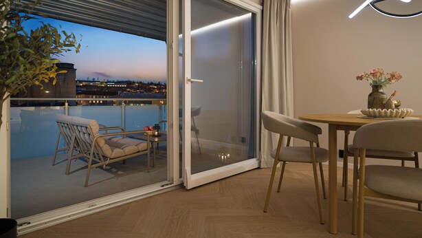 A balcony with a view of a cityscape at dusk, a sliding glass door, and a table with chairs. - Modern 3BR apartment | Free parking | 10 min to centrum (Trondheim)