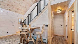 A wooden interior with a staircase, a dining table with chairs, and a hallway. - Quimby Cabin | New Build | Snowmobile Access (Rangeley)