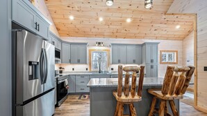 A modern kitchen with grey cabinets, stainless steel appliances, and a wooden ceiling. - Quimby Cabin | New Build | Snowmobile Access (Rangeley)