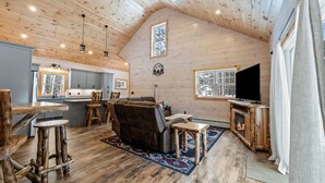 A cozy cabin interior with a wooden ceiling, a fireplace, a TV, and a dining area. - Quimby Cabin | New Build | Snowmobile Access (Rangeley)
