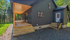 A two-story house with a wooden deck, a small porch, and a front door. - Quimby Cabin | New Build | Snowmobile Access (Rangeley)