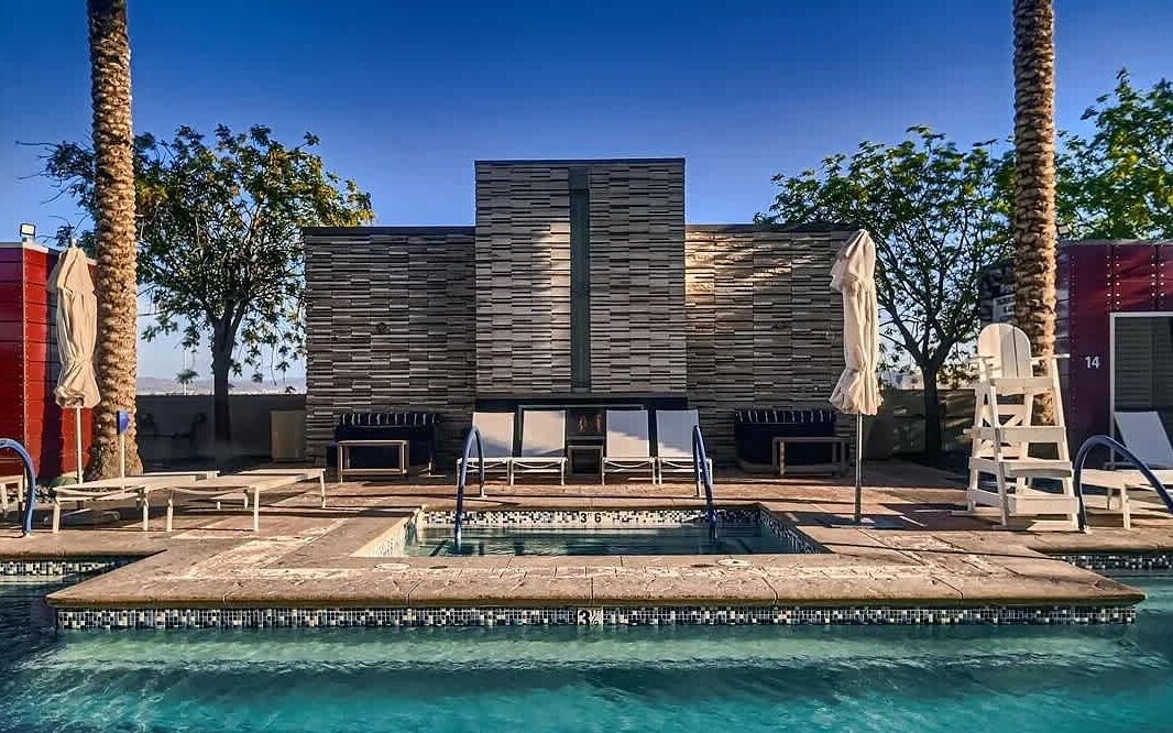 Un espace piscine comprenant une piscine rectangulaire, des chaises longues et des palmiers.