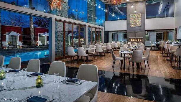 Un espace repas moderne avec vue sur la piscine, de grandes fenêtres et une cheminée centrale.