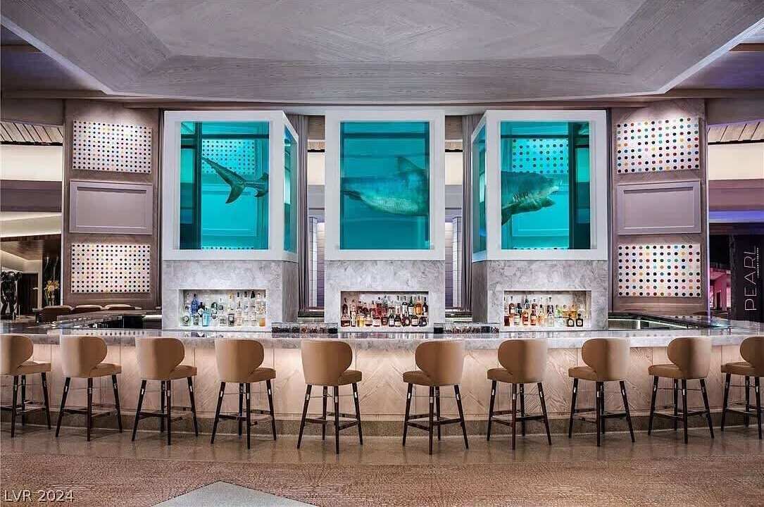 A bar area with a modern design, featuring a central bar counter, multiple seating options, and a large aquarium with fish.