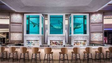 A bar area with a modern design, featuring a central bar counter, multiple seating options, and a large aquarium with fish.