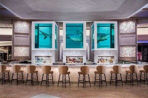 Ein Barbereich mit modernem Design, mit einer zentralen Bar, verschiedenen Sitzgelegenheiten und einem großen Aquarium mit Fischen.