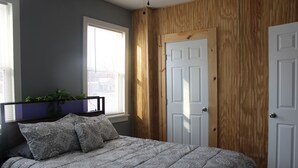 Un dormitorio con cama, ventana, puerta y una planta.