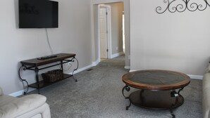Una sala de estar con una televisión de pantalla plana montada en la pared, una mesa de centro redonda, un sofá y una pequeña mesa auxiliar de madera con una cesta.