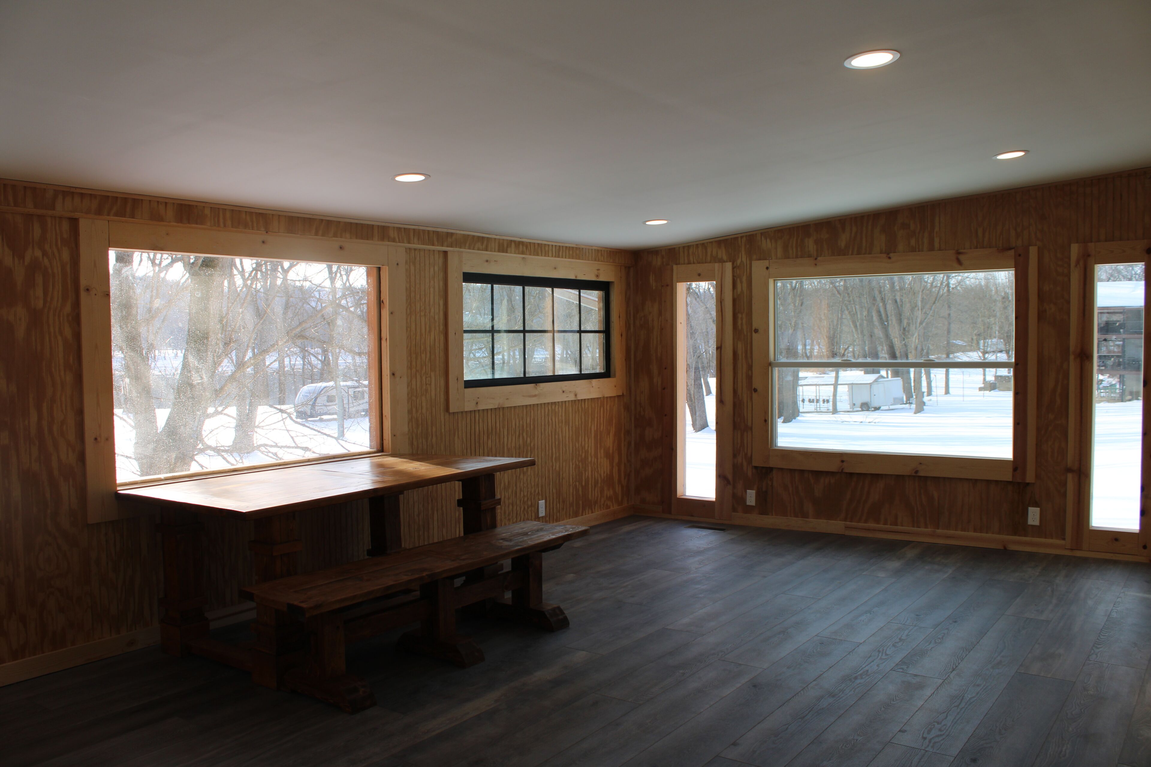 A spacious room with large windows, a wooden bench, and a wooden table.