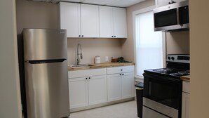 Una cocina con armarios blancos, un refrigerador de acero inoxidable, un microondas y una estufa.