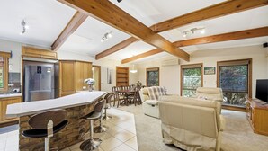 A modern kitchen with a central island, wooden beams, a dining area with a table and chairs, and a living room with a sofa and TV. - Huge 5 Bed Party House: Pool/Renovated Tram/Bar/Games Room/Family Stay (Clyde)