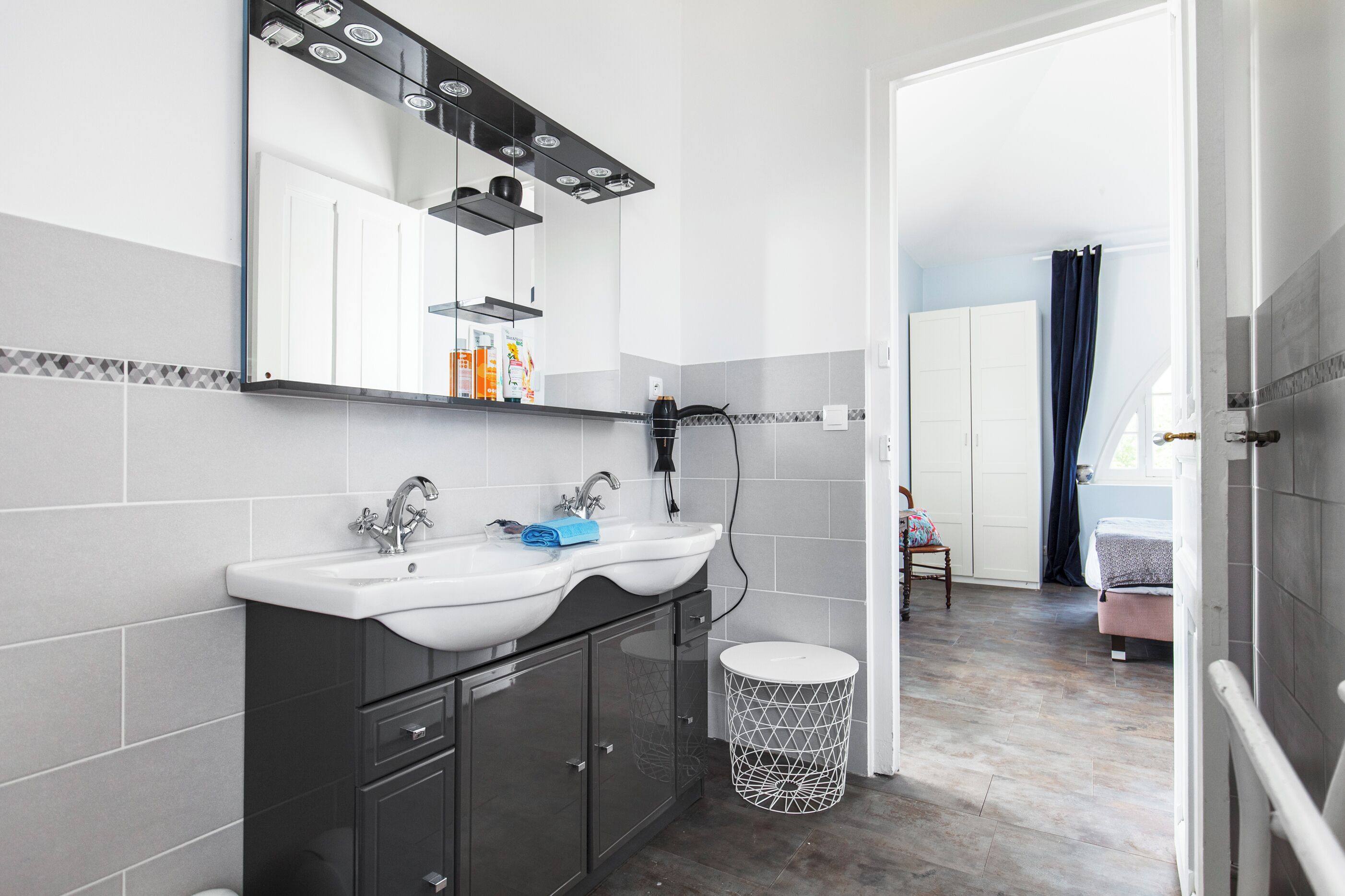 A modern bathroom with a white sink, dark cabinets, a mirror, and a small trash bin.