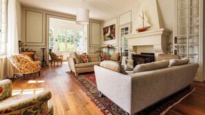 A spacious living room with a fireplace, a sofa, a patterned armchair, and a large window.