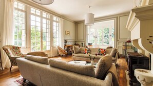 A spacious living room with a sofa, armchairs, a fireplace, and large windows.