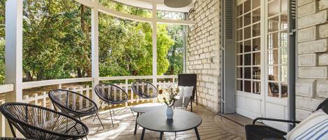 A covered patio with wicker chairs, a table, and a hanging light fixture.