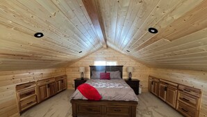 Une chambre avec un plafond en pente, des murs en bois, un lit recouvert d’un jeté rouge, des tables de chevet et des placards intégrés.